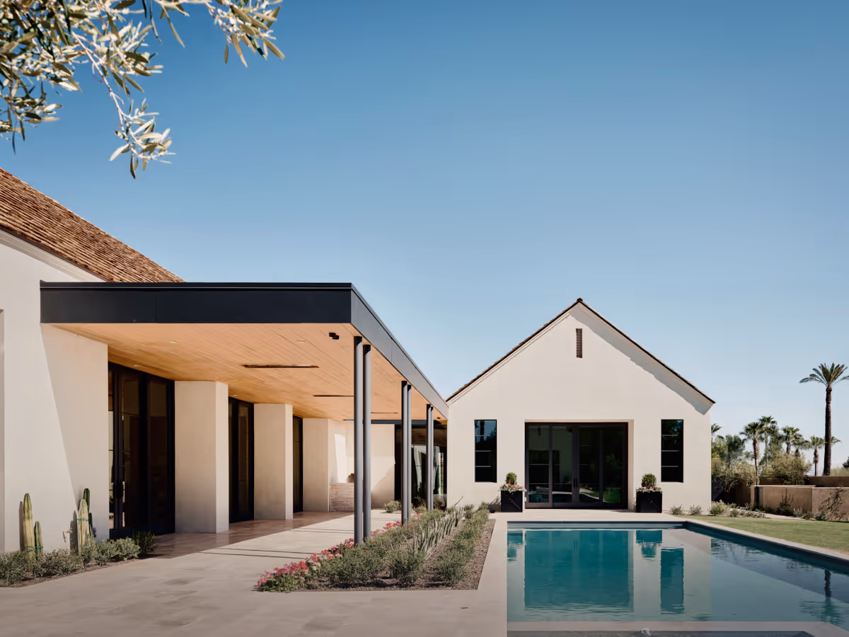 Axis view across the linear pool toward a stucco gable roof anchoring the far end, by The Ranch Mine