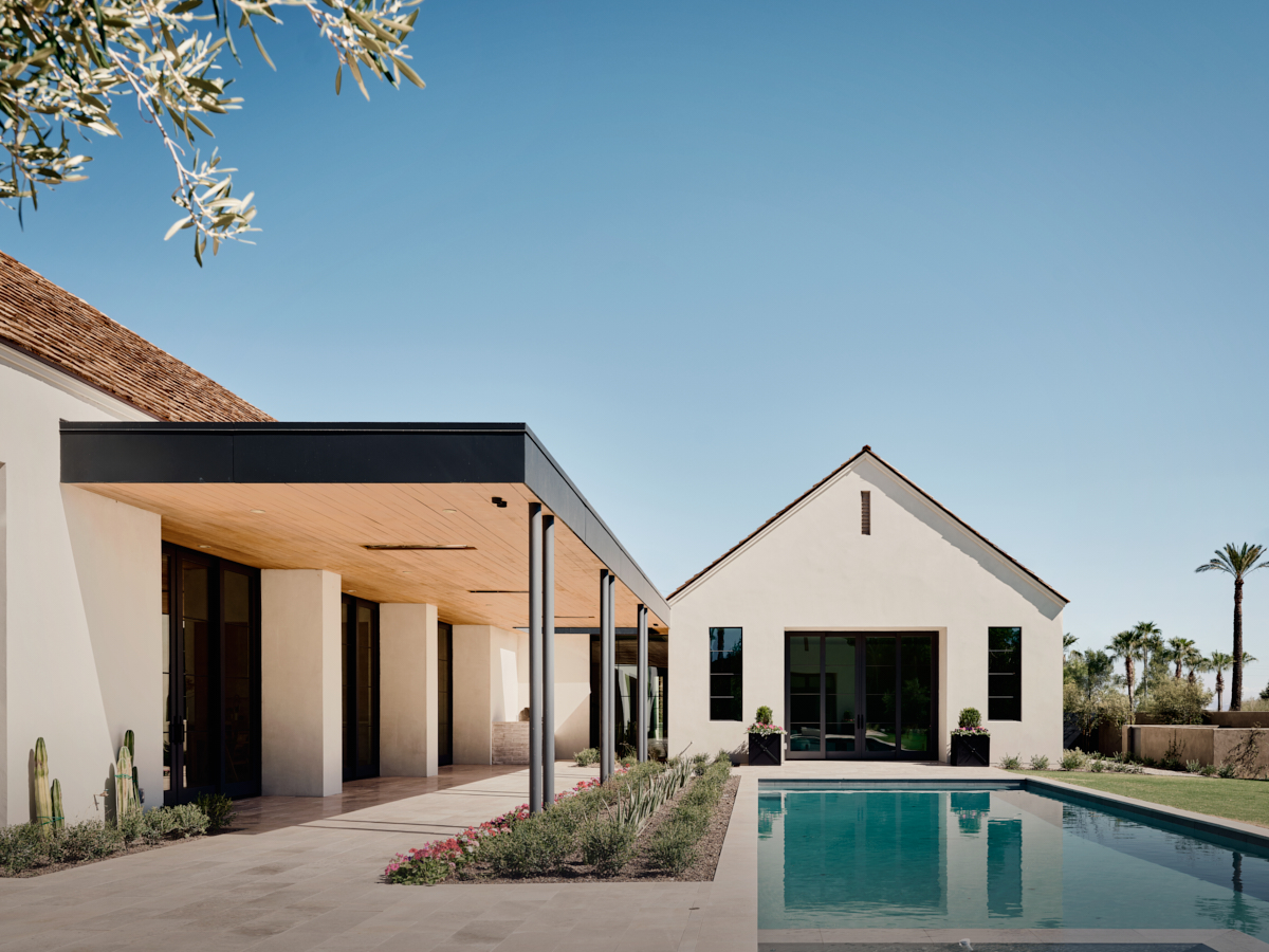 Axis view across the linear pool toward a stucco gable roof anchoring the far end, by The Ranch Mine