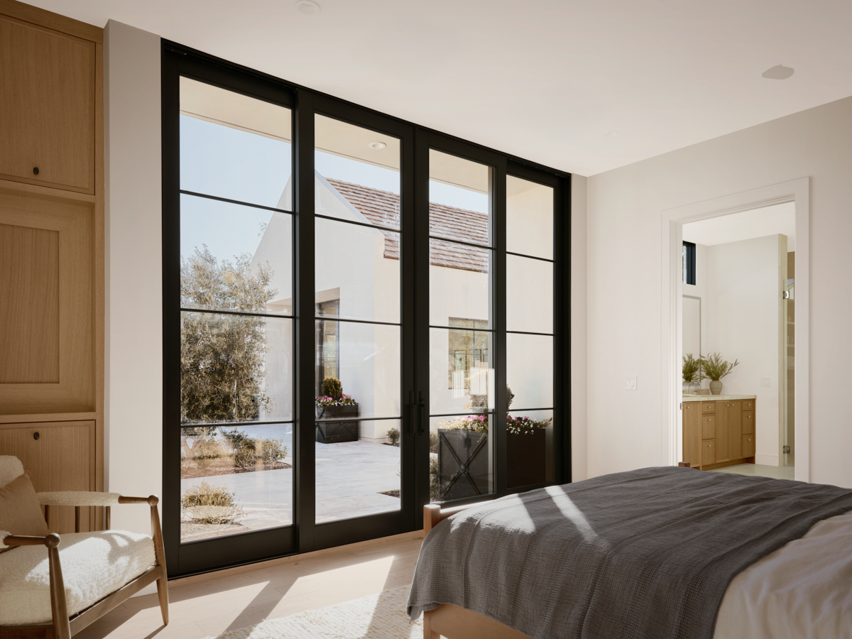 Primary suite looking to the courtyard through black framed doors, calm materials, by The Ranch Mine