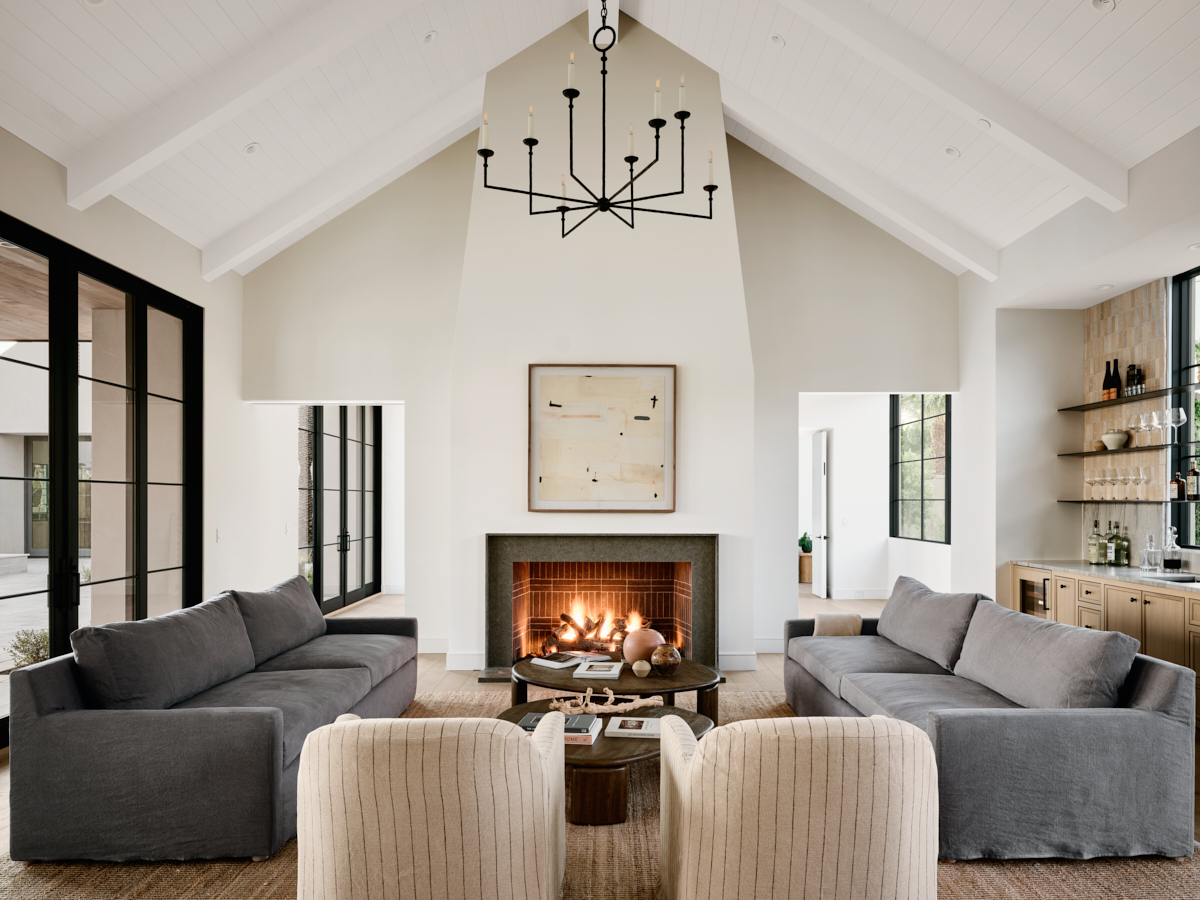 Central fireplace anchoring a cozy living room with white wood beams on the ceiling by The Ranch Mine