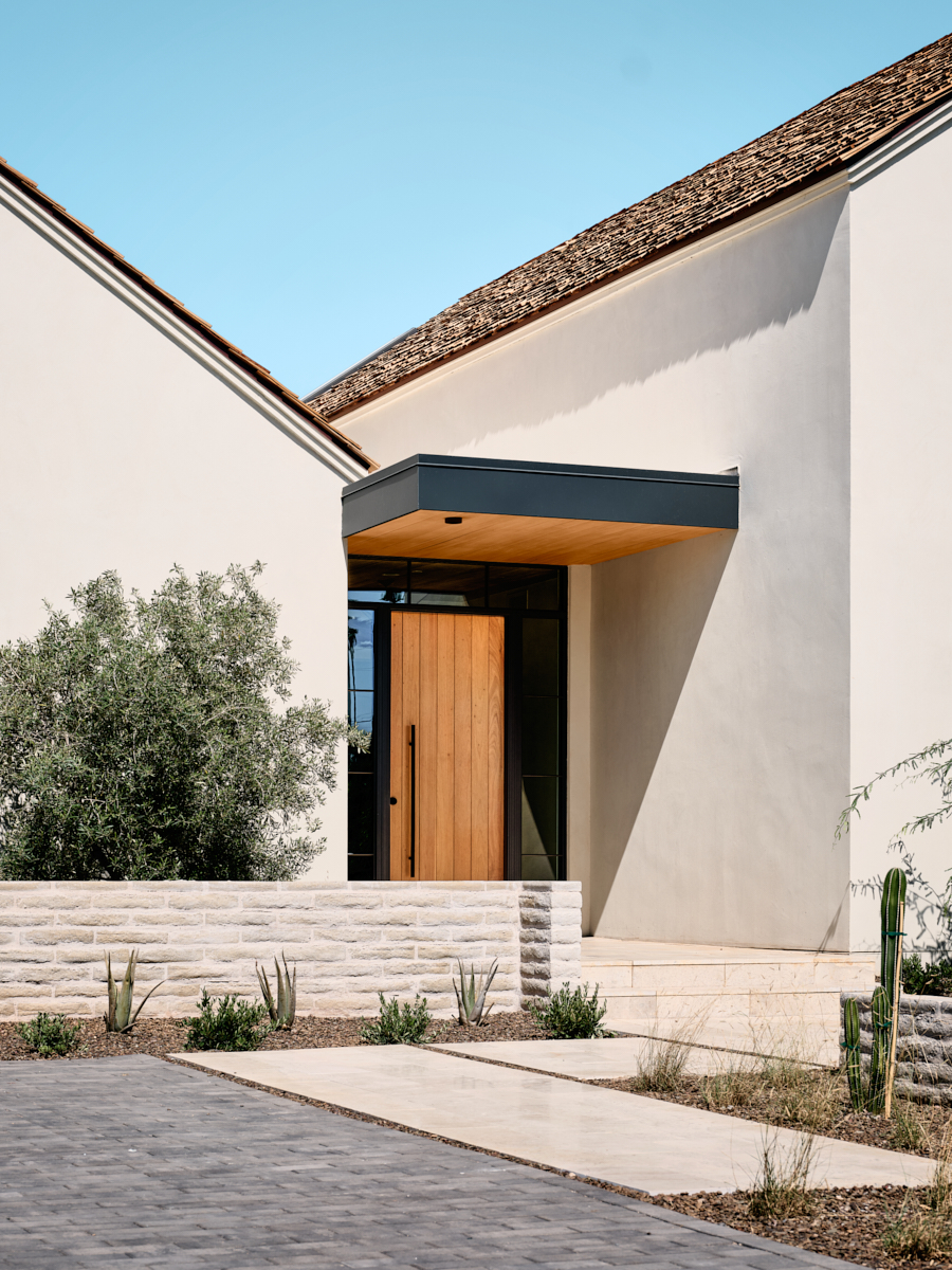Entry court with precise stucco forms and desert planting leading toward the porch, by The Ranch Mine