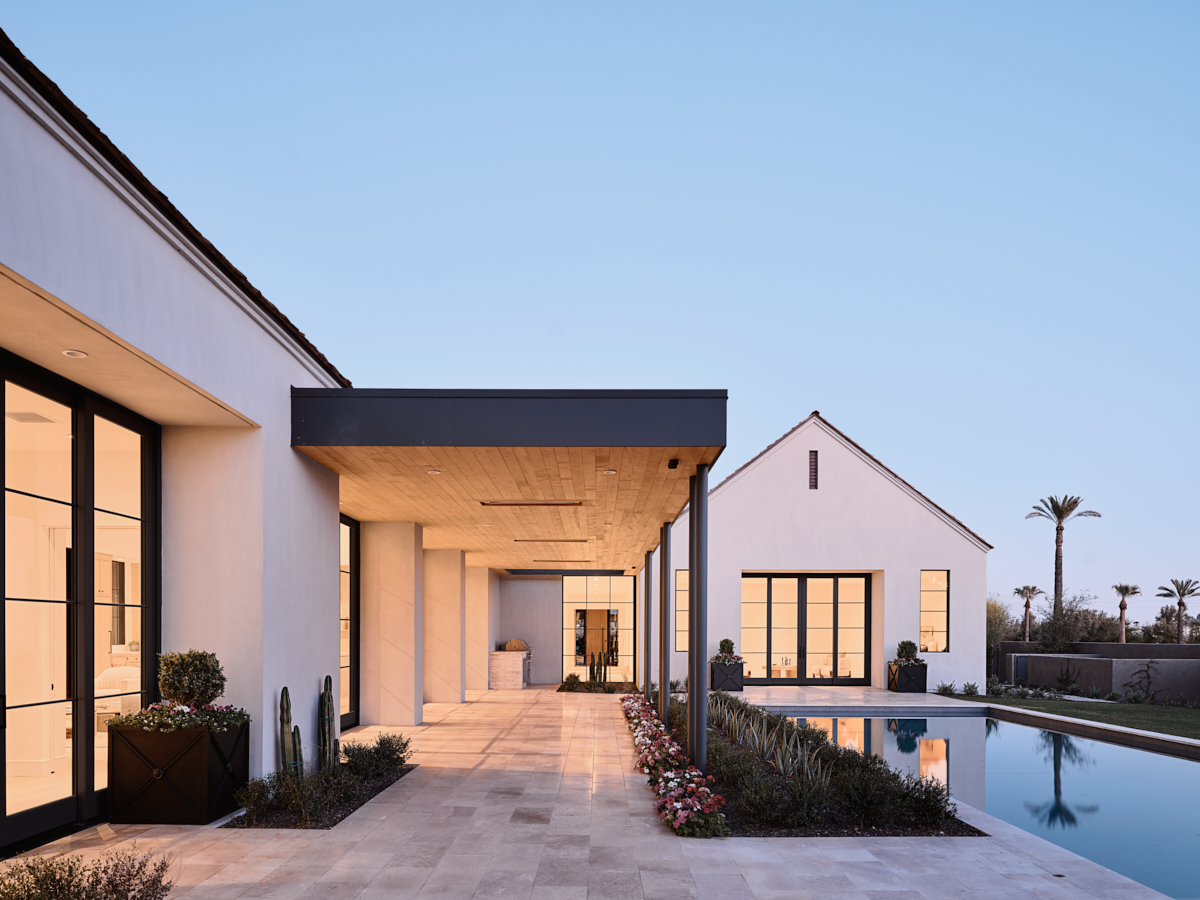 Twilight view of the compound, gabled pavilions linked by a shaded walk around the water court, by The Ranch Mine