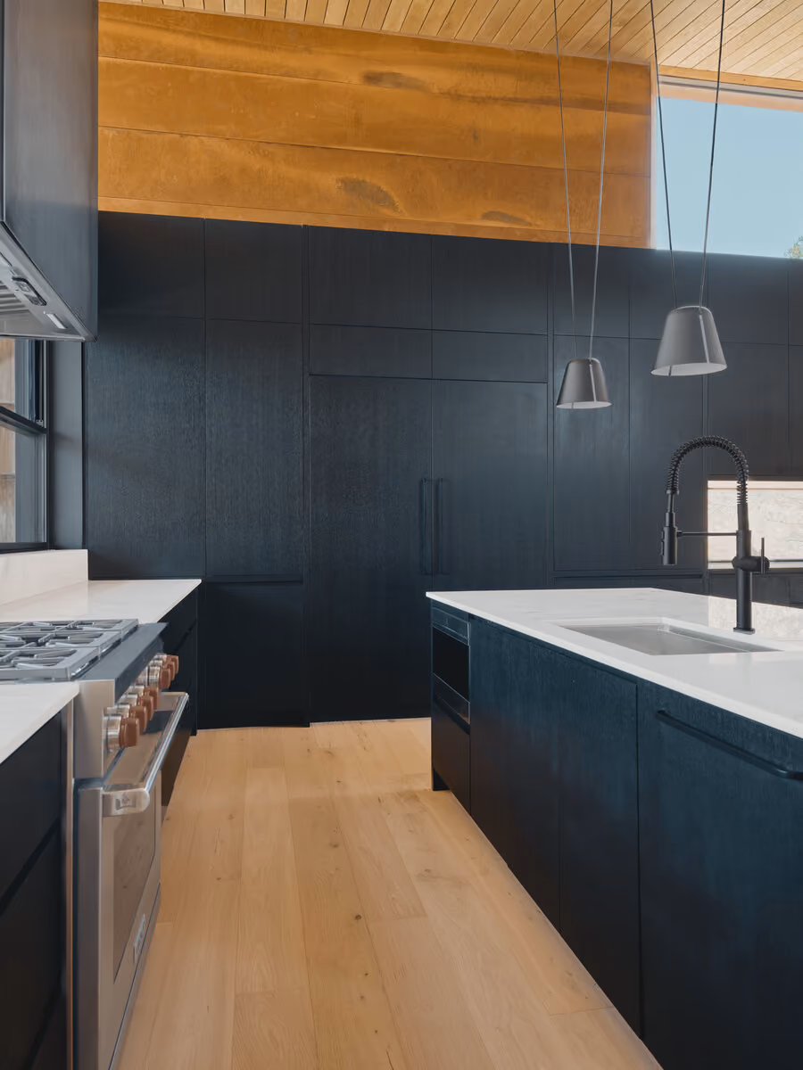 Black cabinetry kitchen with marble counters, gas range and pendant lights under a hemlock ceiling