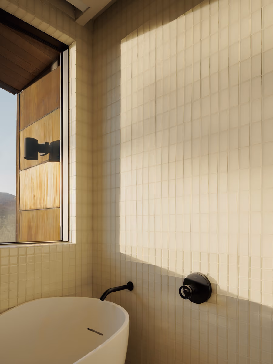 White tile bath detail with a matte black tub filler and evening light raking down the wall