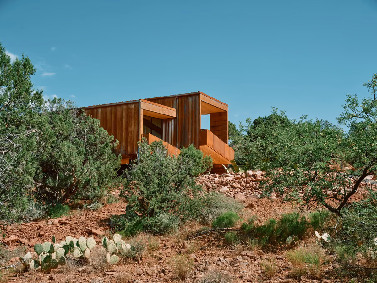 Corten-clad home tucked into a red rock hillside above prickly pear and juniper in Sedona
