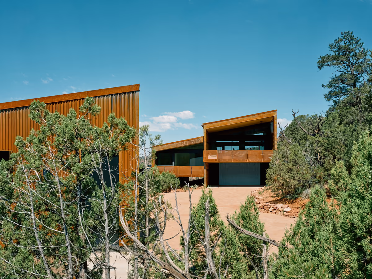Two weathering steel volumes flanking a decomposed granite drive under a clear desert sky