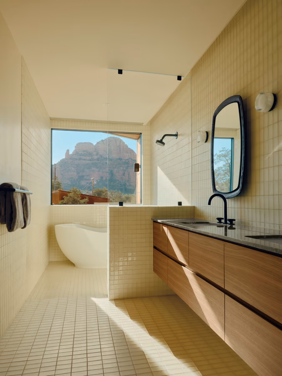 Freestanding soaking tub below a picture window framing Twin Buttes in a white tile bath