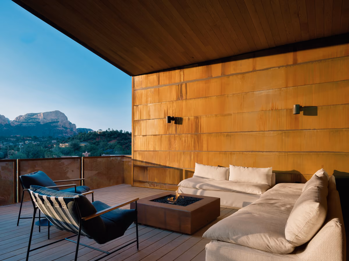 Covered deck at dusk with a lit fire table, sectional and red rock ridgeline in the distance