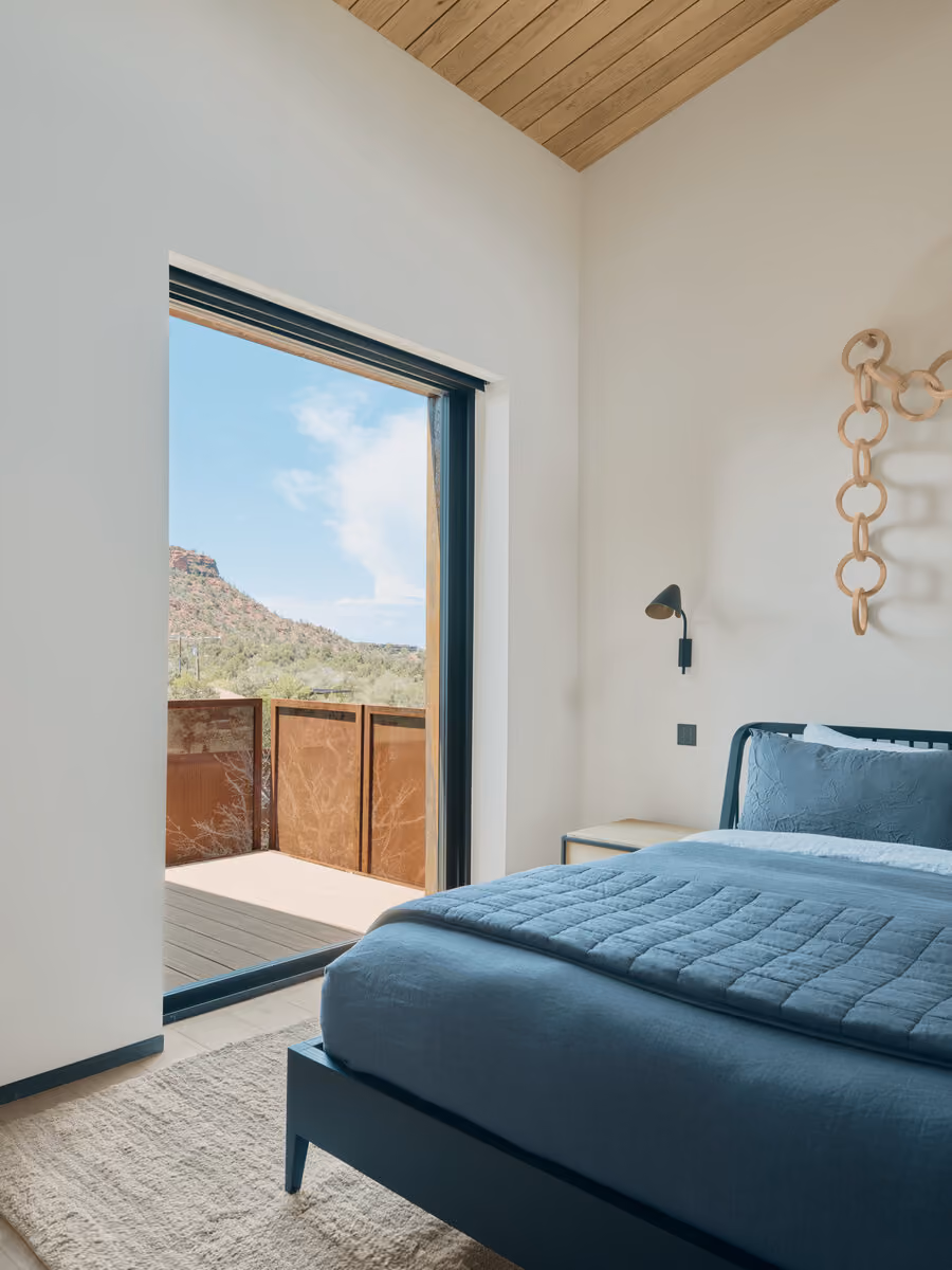 Bedroom with gray bedding and a sliding door opening to a private corten-railed deck