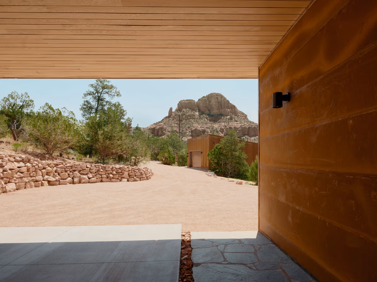 Covered carport framing a red rock butte across the gravel drive