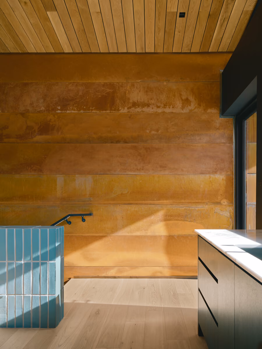 Interior weathering steel wall meeting a hemlock ceiling, with a teal tile stair guard and white oak floors