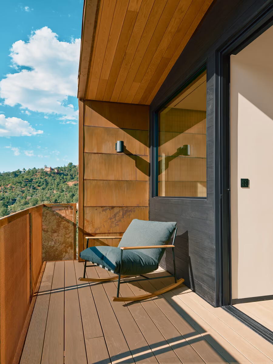 Private bedroom balcony with a gray rocking chair and corten mesh railing above the canyon