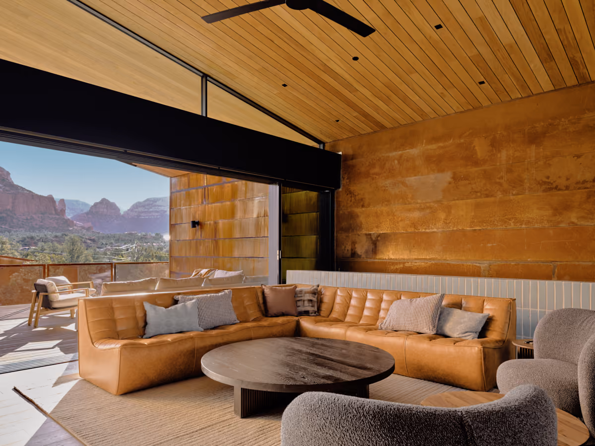 Living room with the glass wall fully open to red rock views beyond the leather sectional