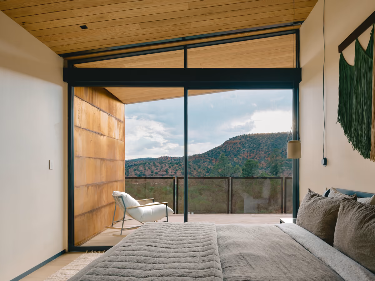 Bedroom with linen bedding opening to a deck and a juniper-covered hillside