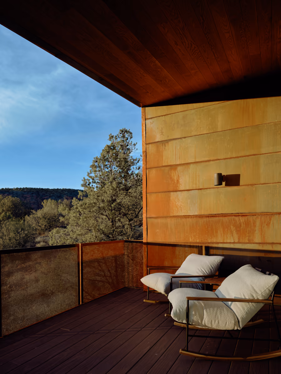 Covered deck at dusk with white rocking chairs, a corten wall and canyon views past the mesh railing