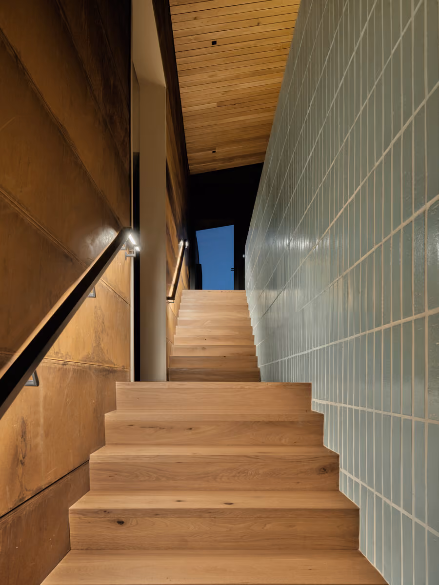 Stair between a weathering steel wall and pale tile, night sky visible at the top