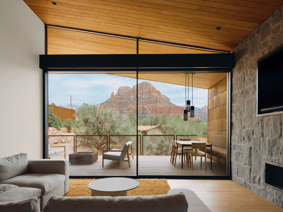 Living room with a stone fireplace wall opening through sliding glass to a deck and red rock butte