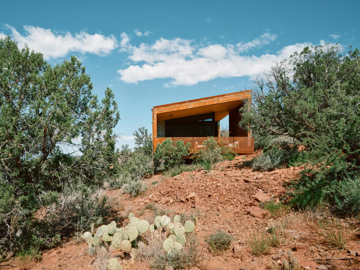 Corten cabin perched on a rocky red slope above prickly pear and juniper