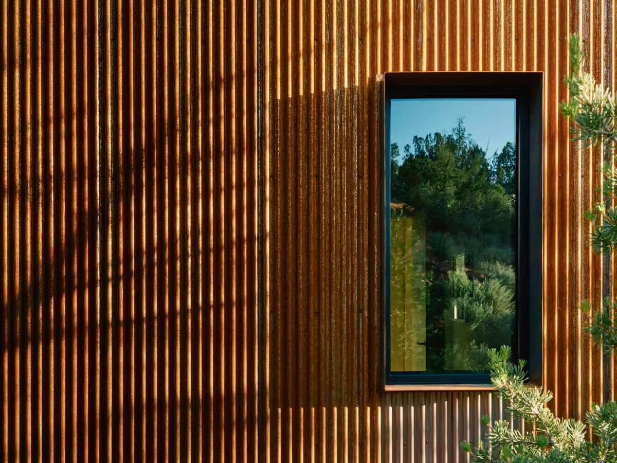 Corrugated weathering steel facade with a tall narrow window catching low evening sun