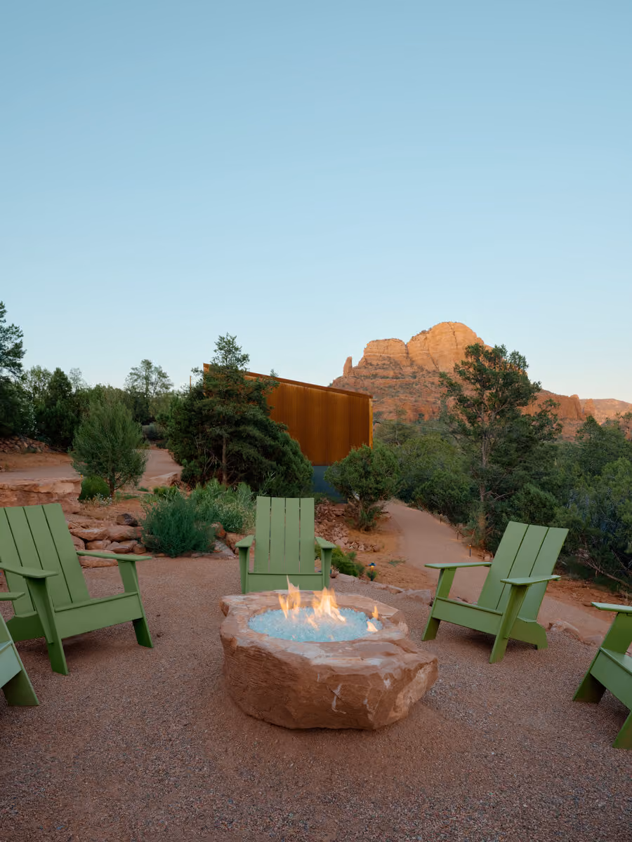 Green Adirondack chairs around a sandstone fire pit with the cabin and a red rock butte beyond