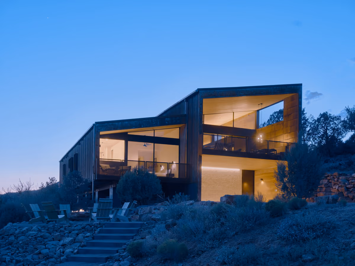 The main house glowing at dusk above the fire pit terrace, upper deck open to the sky