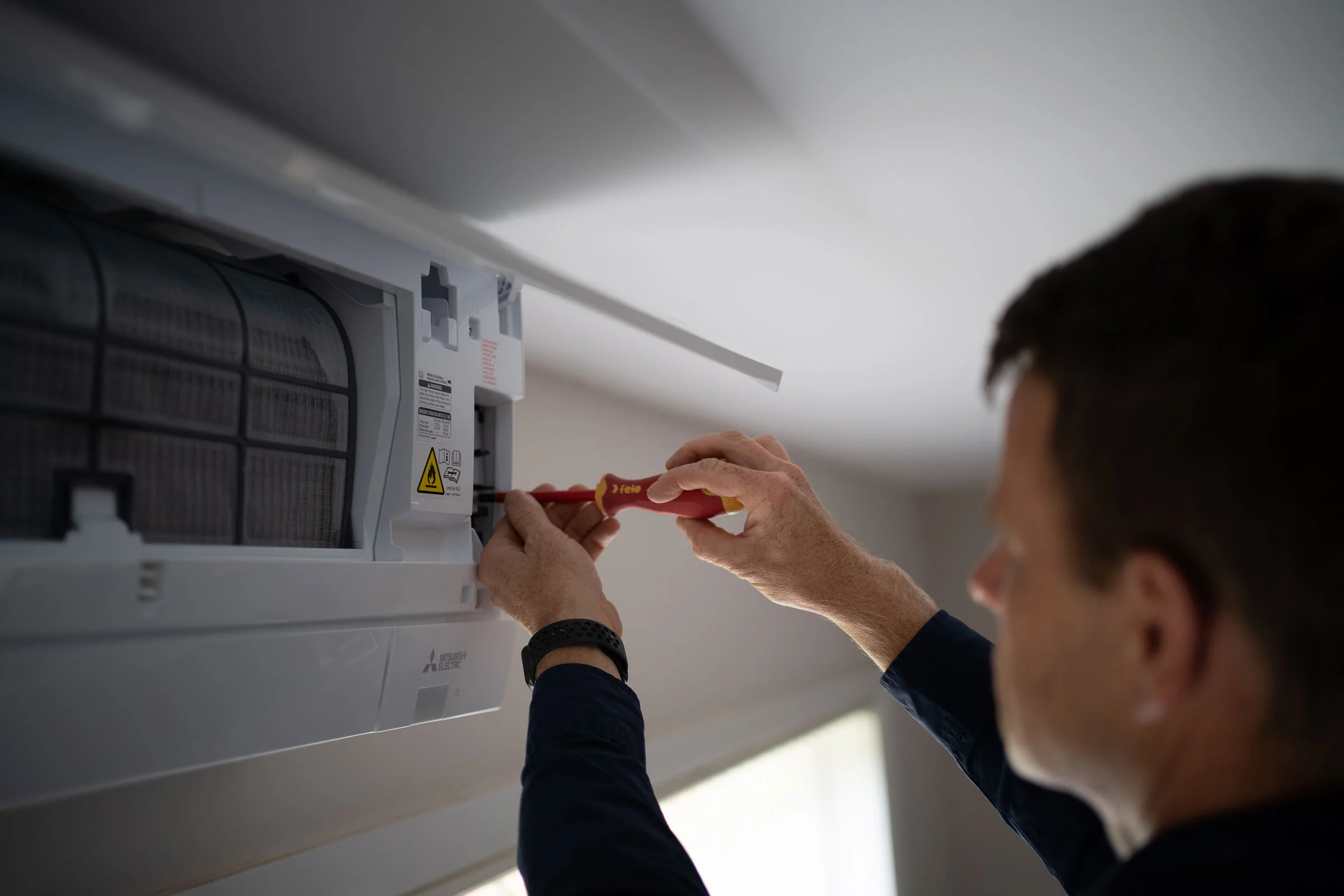 A Renew Air specialist using a screwdriver to repair a wall-mounted air conditioning unit in Port Macquarie.