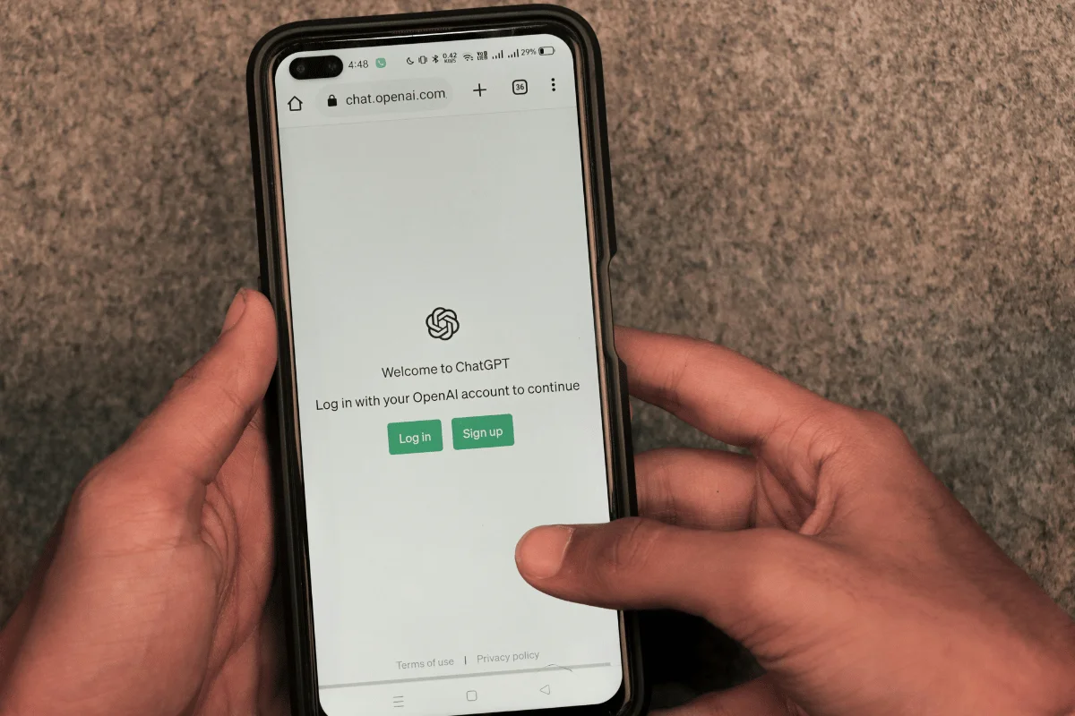 A person holds a smartphone displaying the ChatGPT login screen, featuring options to log in or sign up on a simple background.