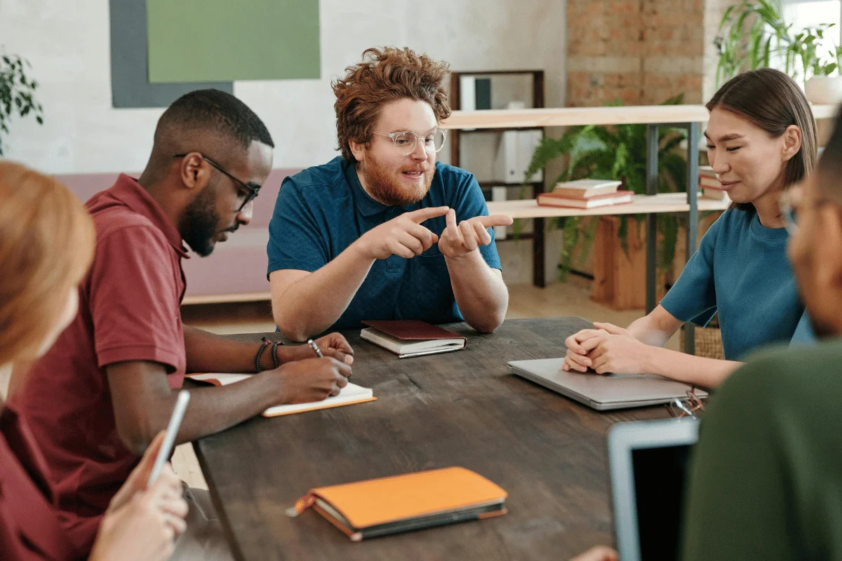 Diverse team meeting around a table as coworkers discuss ideas and take notes in a creative office.