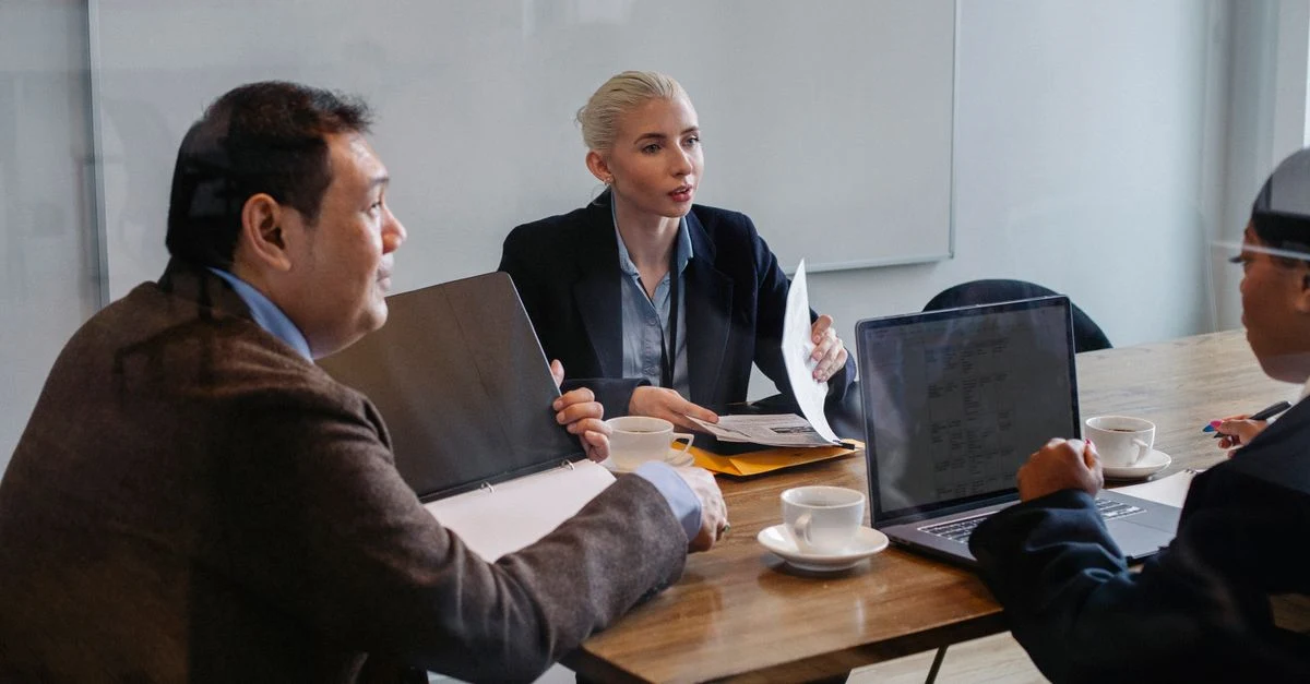 Professionals in business meeting discussing b2b content writing strategy around wooden table with laptops and documents.