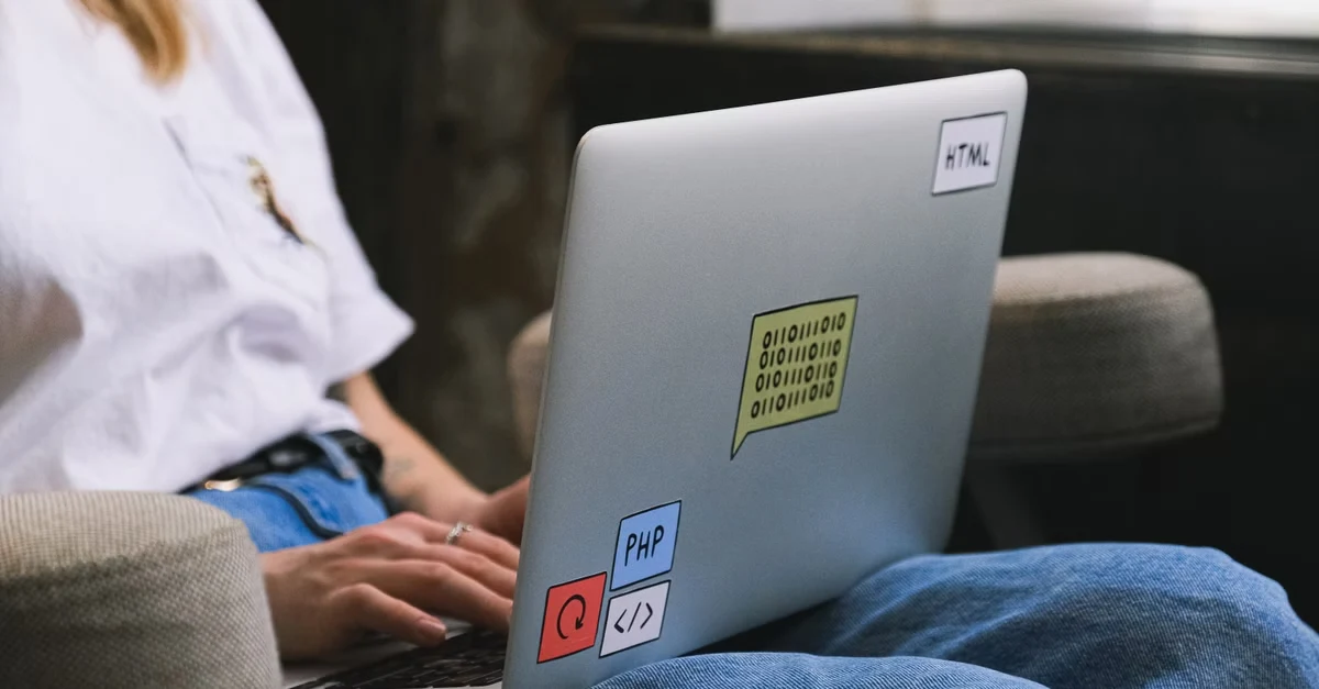 Developer coding on laptop with programming language stickers showing enterprise search trends and technologies.