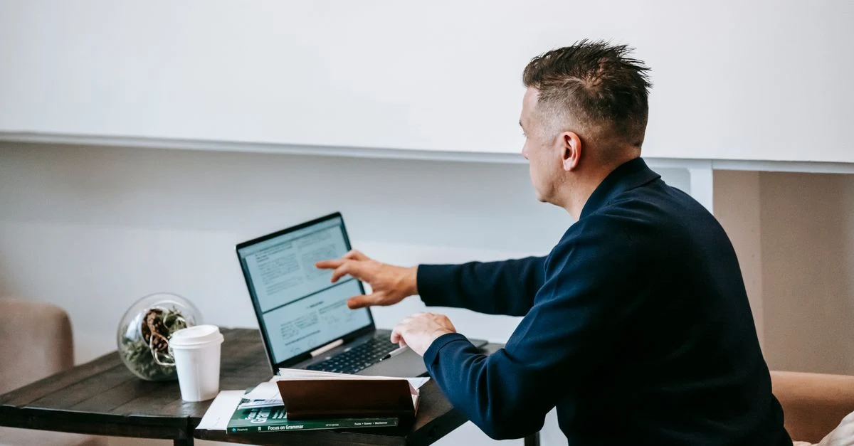 Man typing on laptop at desk while reviewing B2B link building strategy notes and coffee mug nearby.