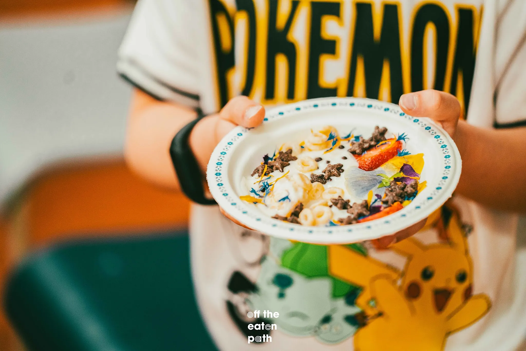 Student holds a yogurt bowl decorated with fruit, cereal, chocolate quinoa puffs, and edible flowers.