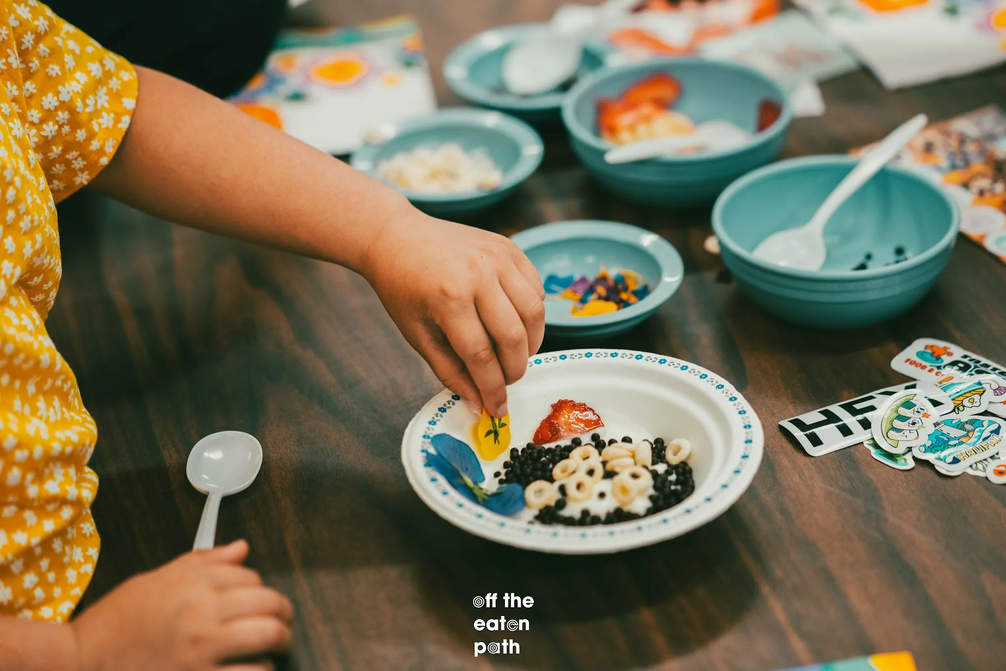 Student decorates a yogurt bowl with fruit, cereal, and edible flowers.