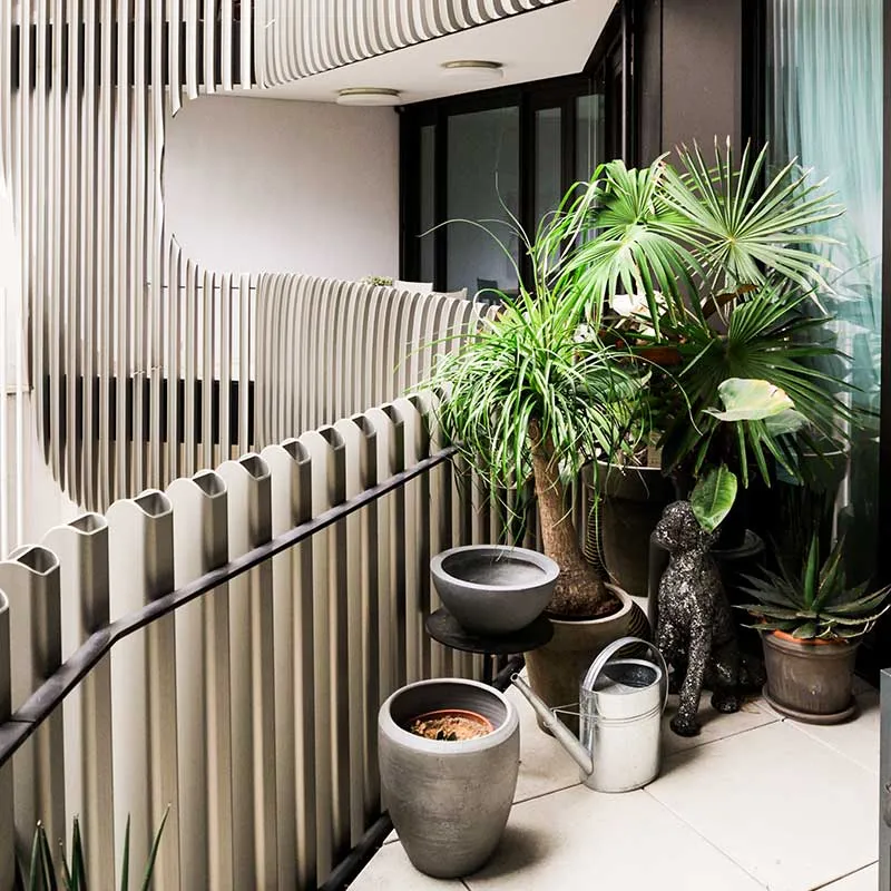 Balcony with potted green plants, a silver watering can, and a decorative dog statue against a modern railing.