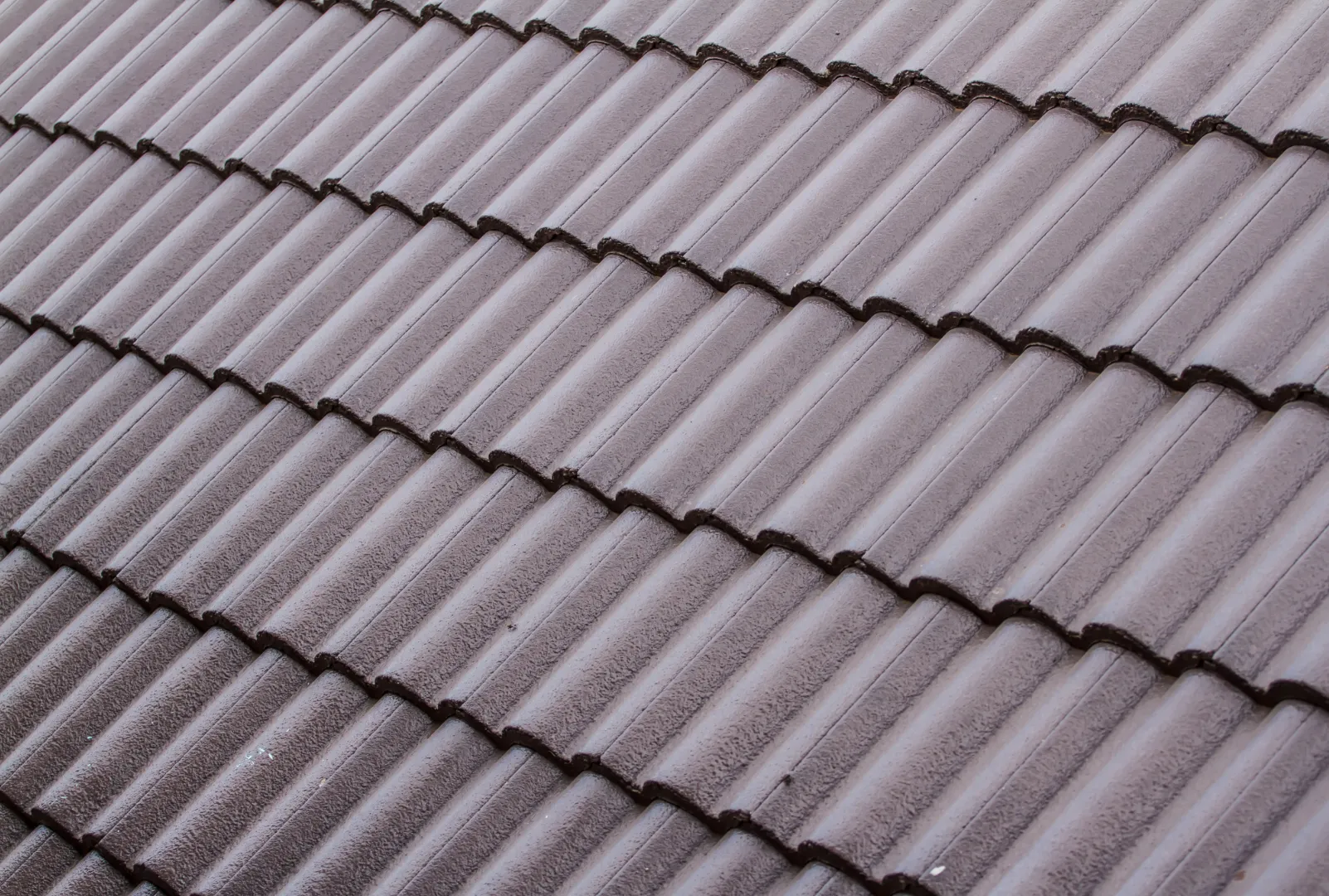 Close-up of gray ceramic roof tiles arranged in neat, overlapping rows, showcasing detailed texture.