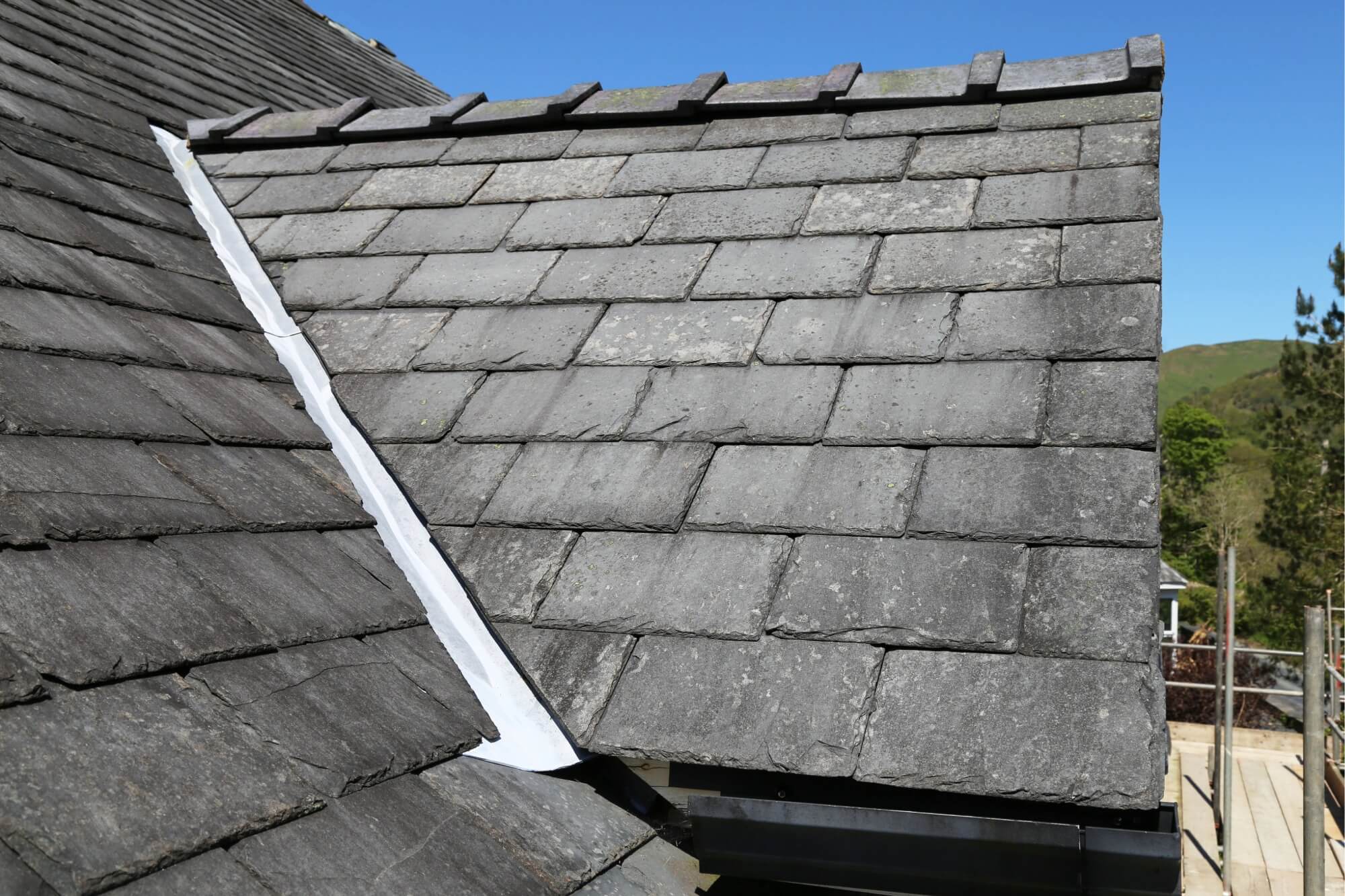 Natural slate roof with flashing detail against a clear blue sky, emphasizing roofing materials and construction.