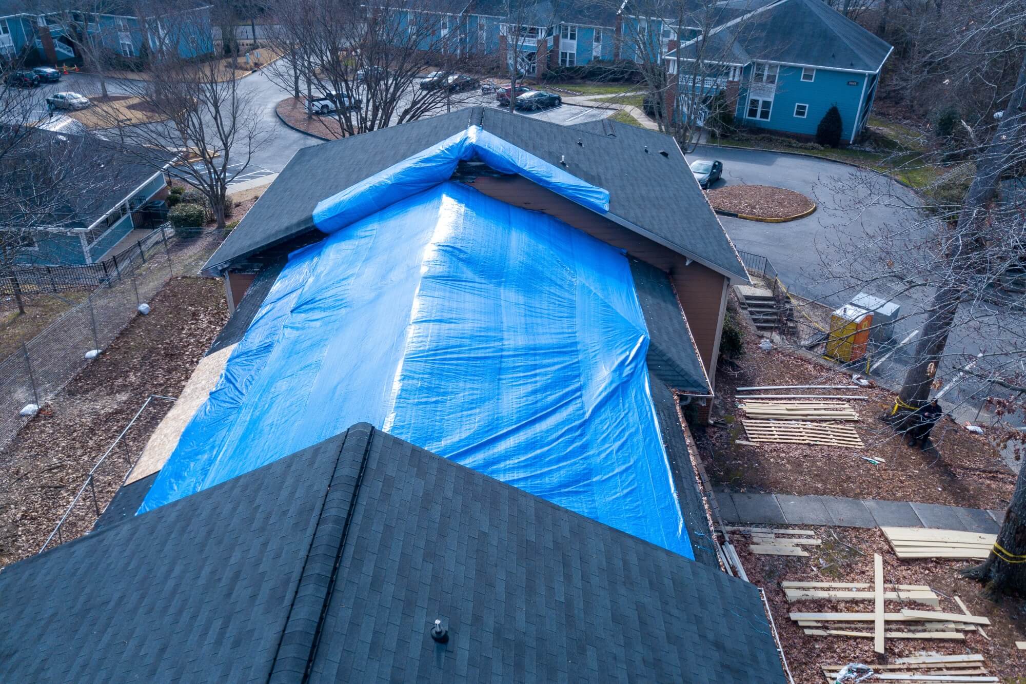 Multifamily roof covered with blue tarp for weather protection during construction in residential neighborhood.