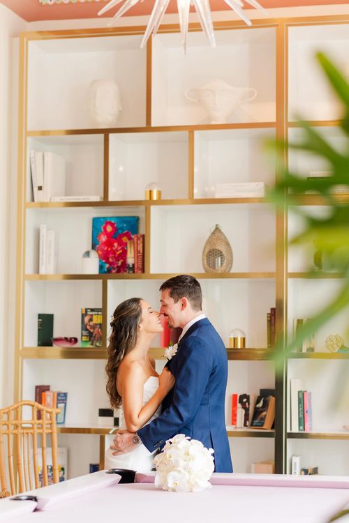 Bride and groom sharing an intimate moment at their wedding reception, with a warmly decorated bar featuring elegant shelving in the background.