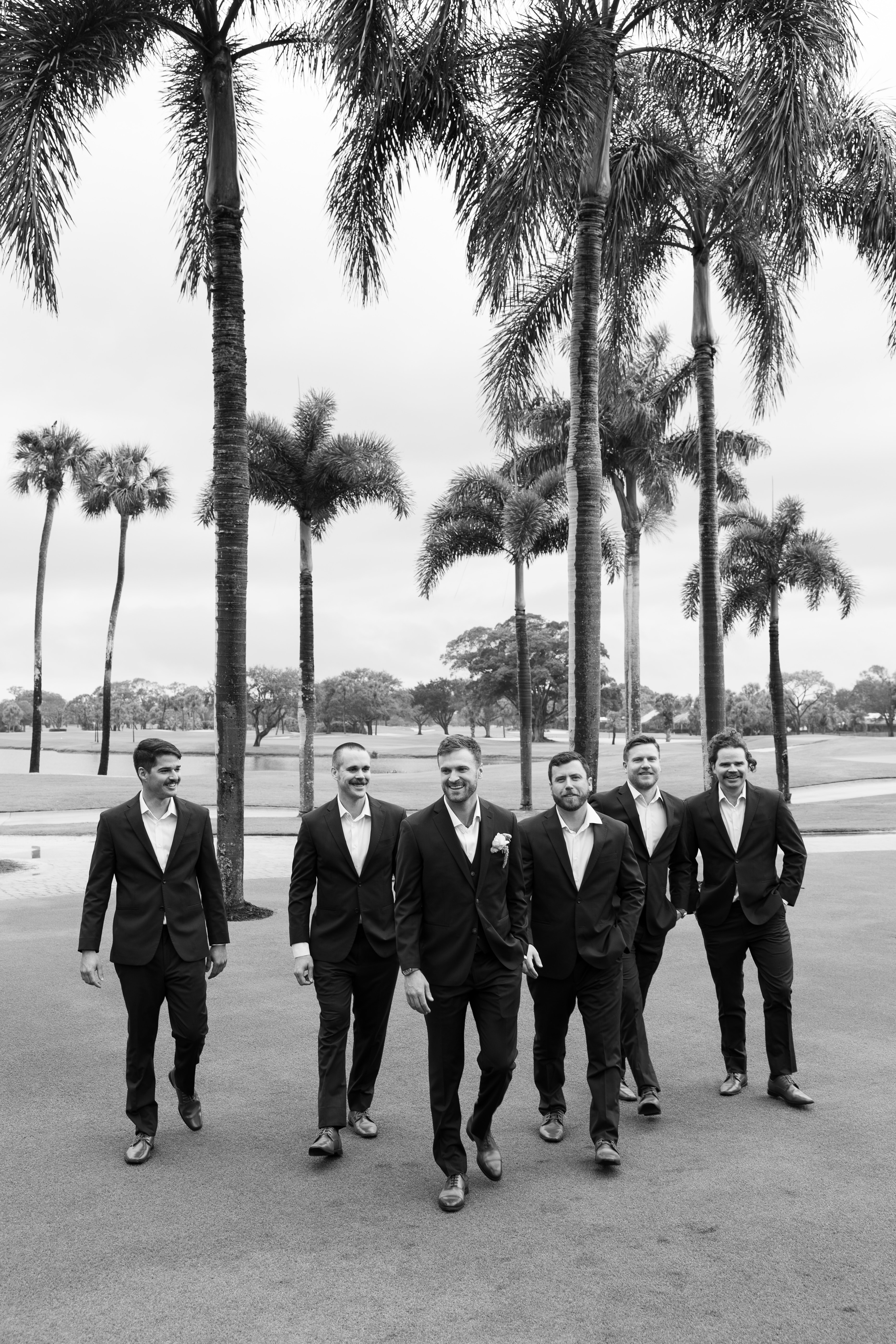 Groomsmen walking together beneath palm trees at Turtle Creek Country Club.