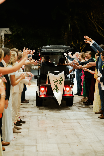 Bride and groom departing their wedding reception in a decorated golf cart.