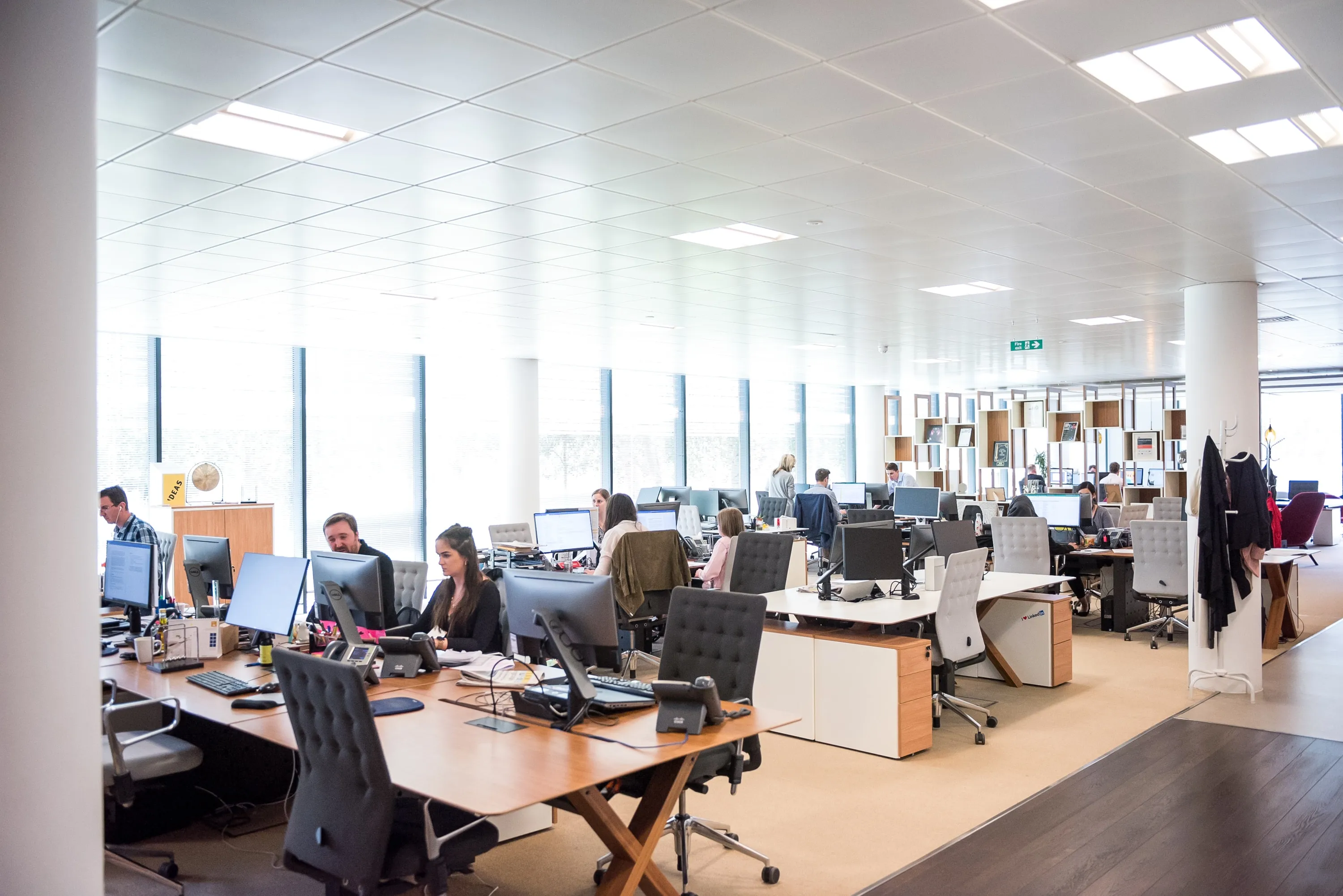 Un bureau open space lumineux avec plusieurs personnes travaillant sur des ordinateurs sur des bureaux en bois.