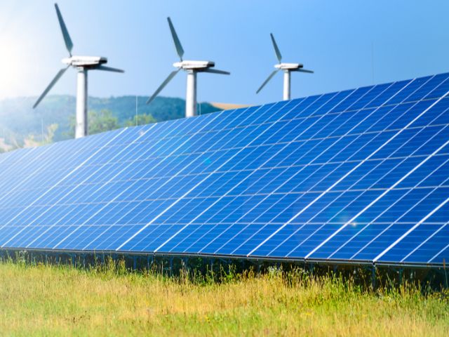 au premier plan, des panneaux solaires, en fond des éoliennes pour inciter à investir dans les énergies renouvelables