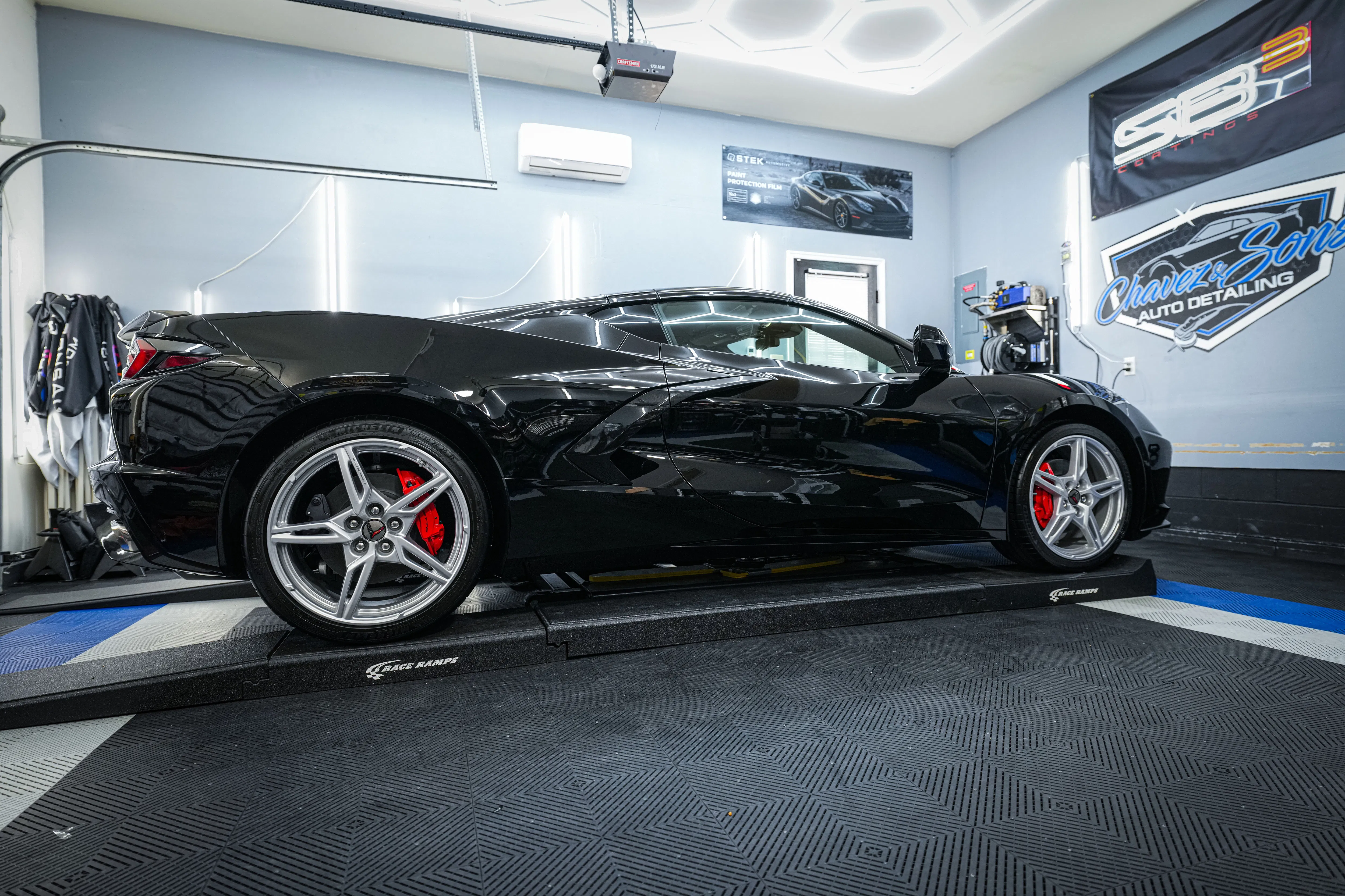 A black sports car with red brake calipers is showcased on Race Ramps in the Chavez Auto Detailing shop, highlighting a flawless, glass-like finish from an SB3 Trinity ceramic coating.