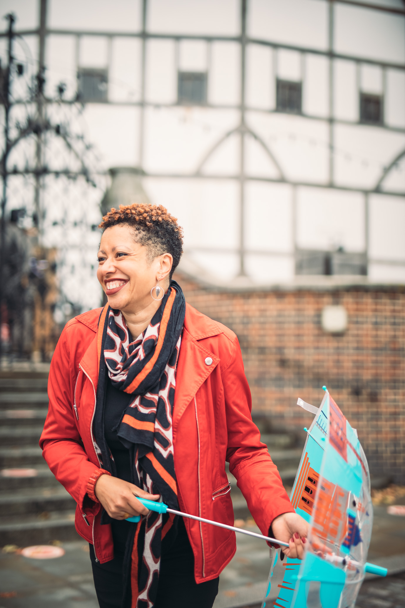 Annette in a bright red jacket laughing and holding an umbrella with the Shakespeare's Globe theatre in the background