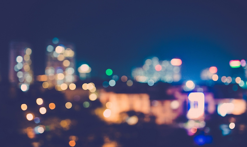 Blurred bokeh lights of a city skyline at night, symbolizing vision, future opportunities, and modern technology focus.