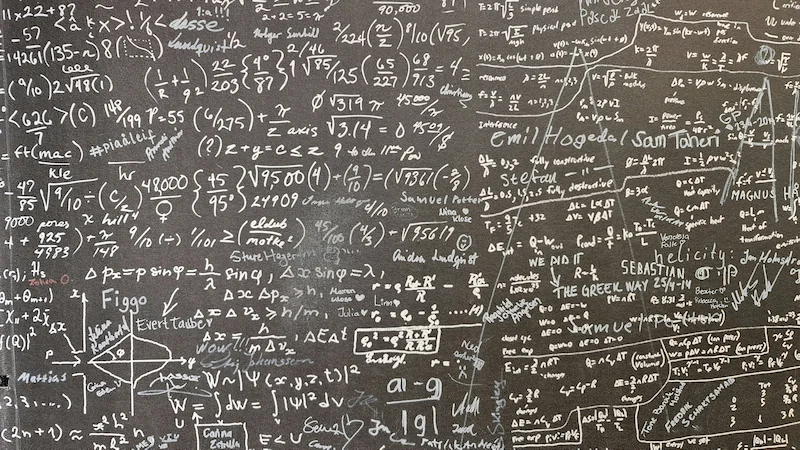 A chalkboard covered in dense mathematical equations, physics formulas, and diagrams, symbolizing complex problem-solving, and analytical thinking
