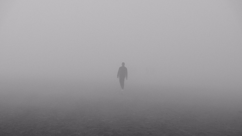 A lone figure walking through dense, heavy fog, symbolizing navigation through uncertainty, overcoming challenges, and finding clarity in complex projects.