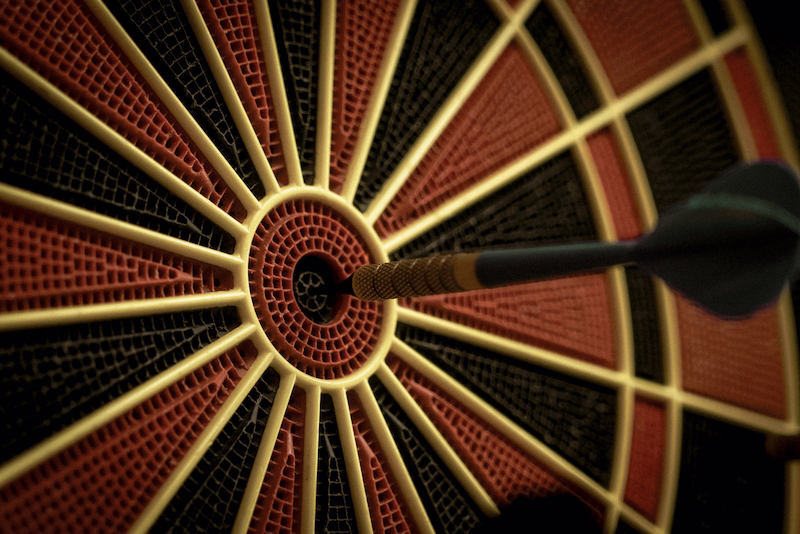 A dart hitting directly in the center of a dartboard bullseye, symbolizing precision, hitting project targets, and achieving goals