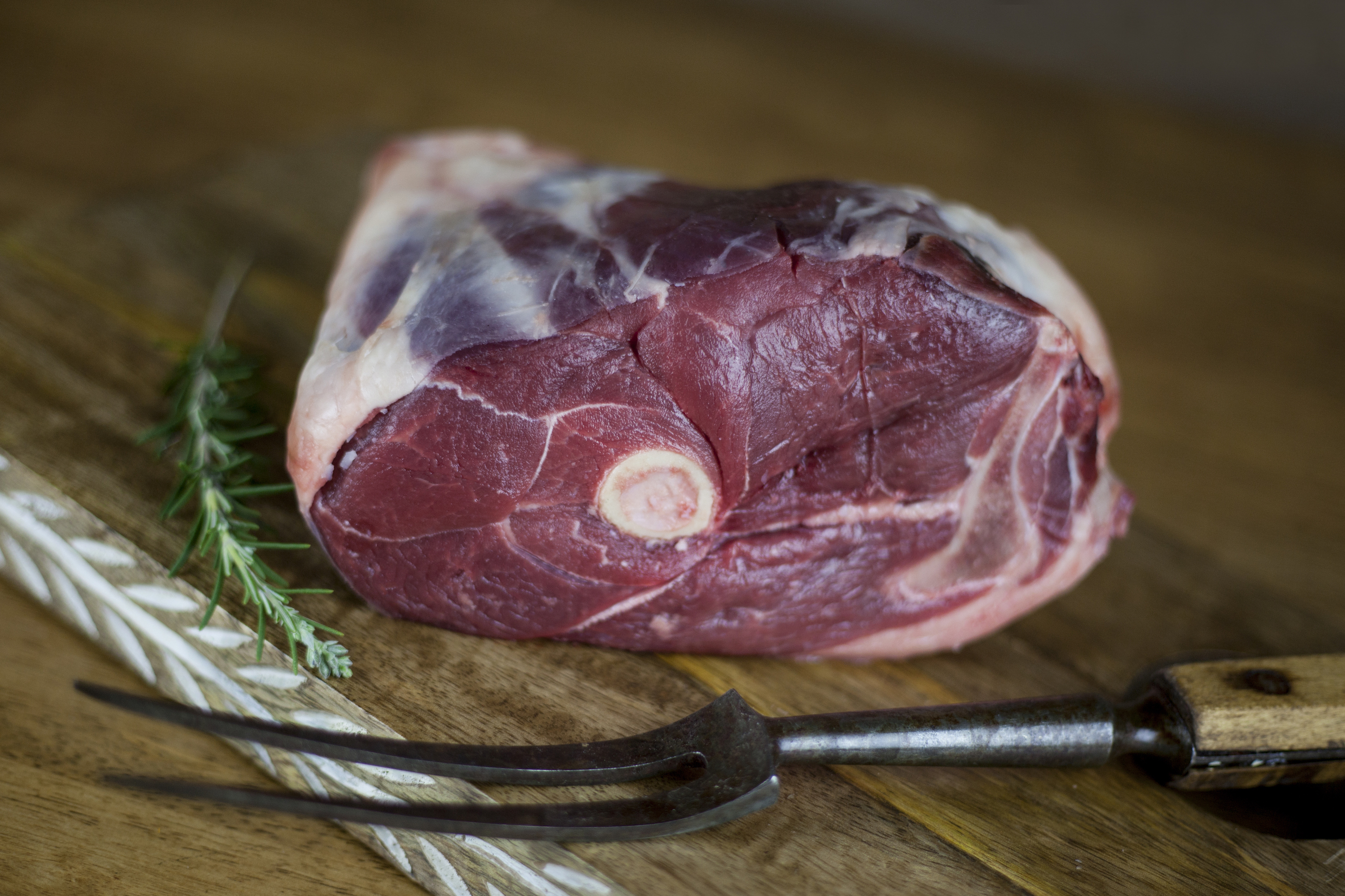 Raw grass-fed lamb leg on a cutting board from Central Grazing Company with rosemary.