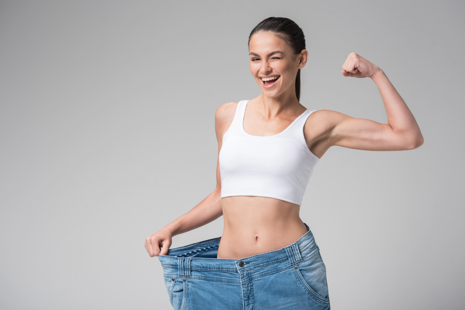 Woman in loose jeans, flexing bicep, smiling.